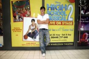 Doyle infront of a poster of himself advertising the UK Premiere of High School Musical Two